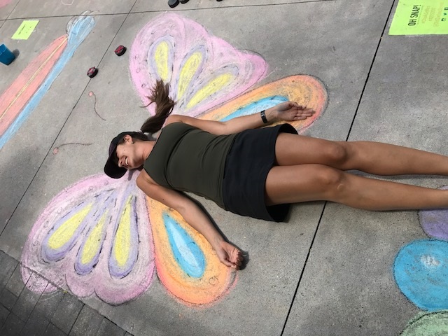 woman lying in a chalk drawing of a butterfly so it looks like she has wings